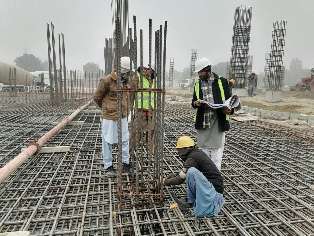 Construction workers and engineers at a site in Bahāwalnagar, Punjab, Pakistan, inspecting metal framework.
